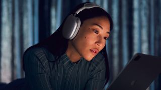 A woman wearing the apple airpods max headphones in a dark room while looking at a screen