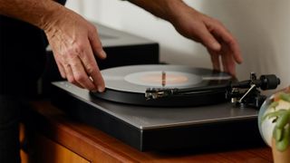 Cambridge Audio Alva TT V2 on sideboard, with man placing a record on the turntable