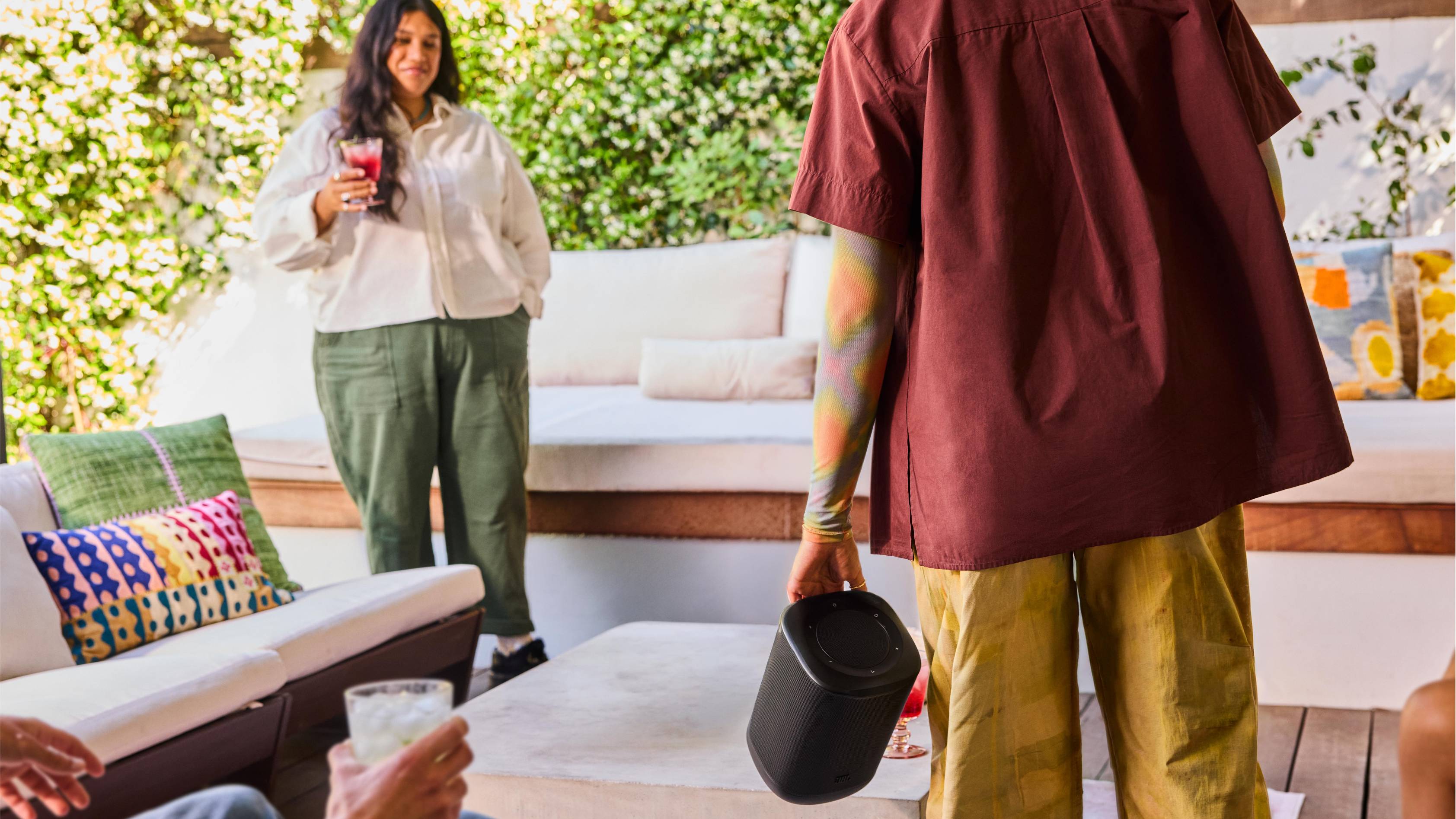 The JBL Cove P1 in someone's hand, as they stand across the yard from someone else.