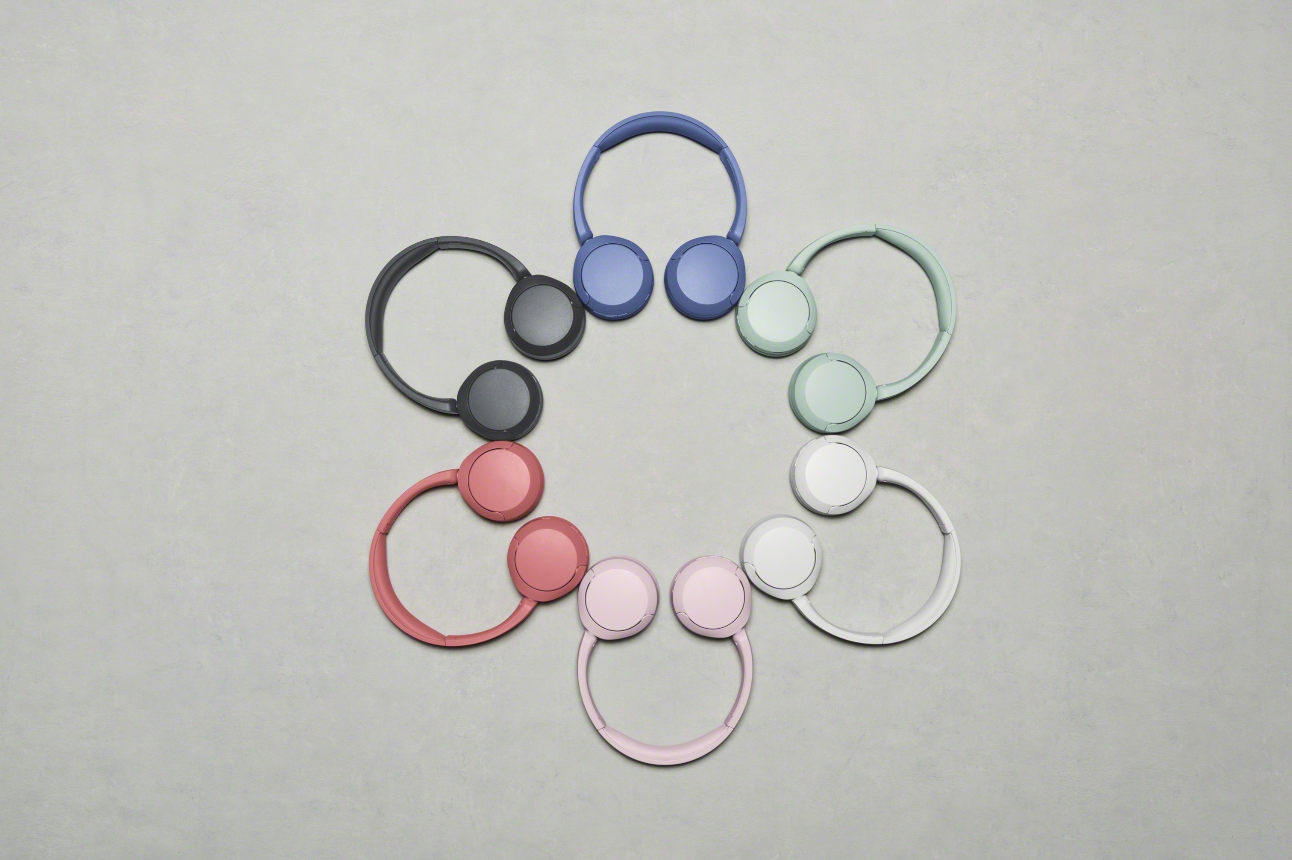 Sony WH-CH530N headphones in different colors, arranged in a circle to form a flower shape, on a gray floor