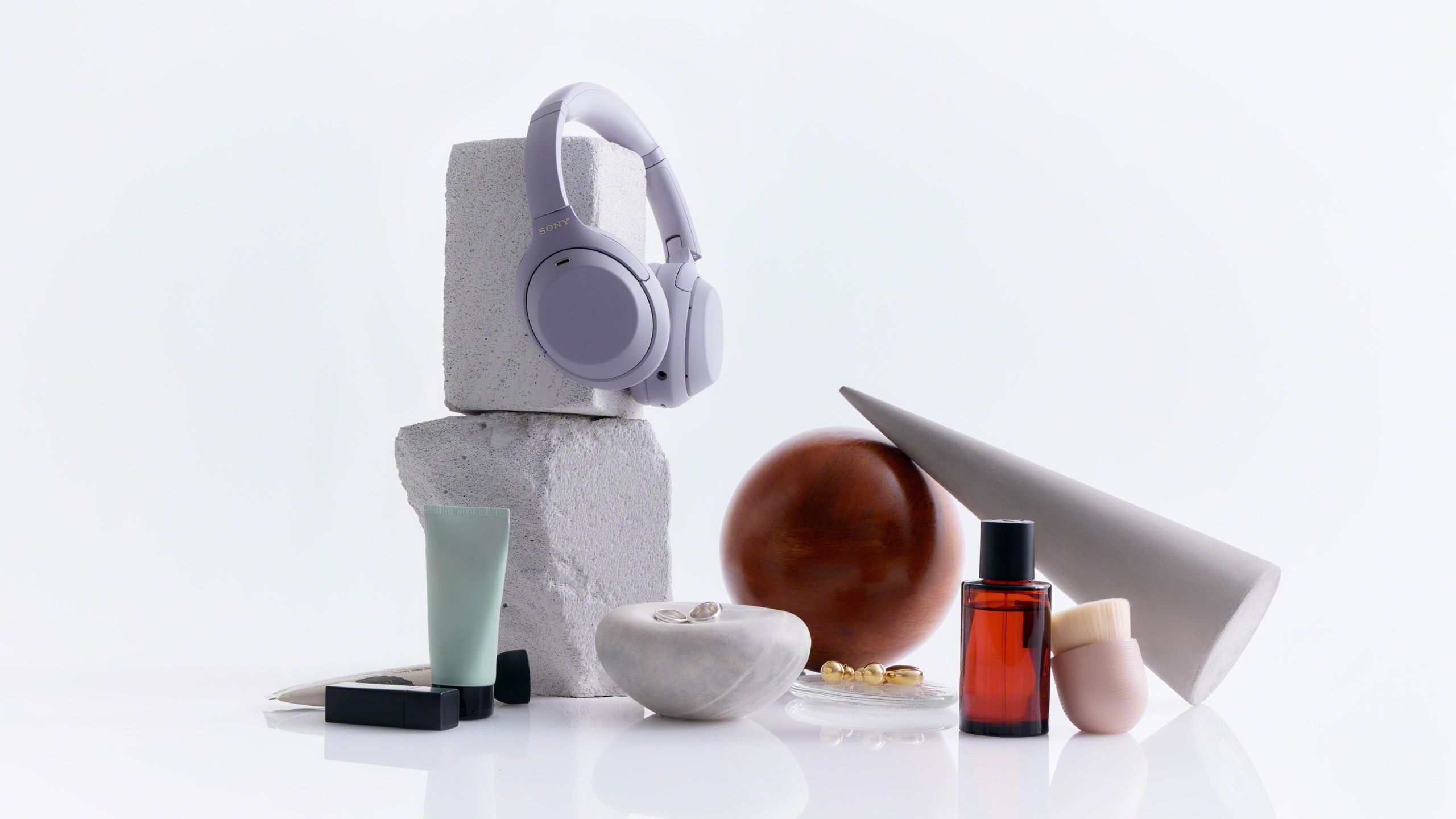 Sony WH-1000XM4C on a grey plinth, with a few other items in the frame, including a perfume bottle